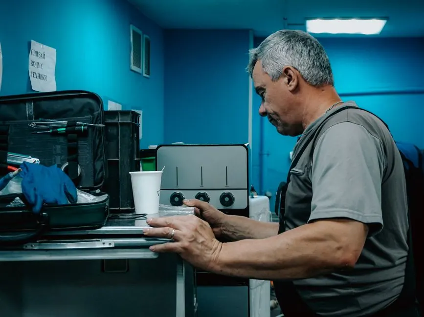 A male technician works on a machine in an industrial environment, focused on adjusting controls.
